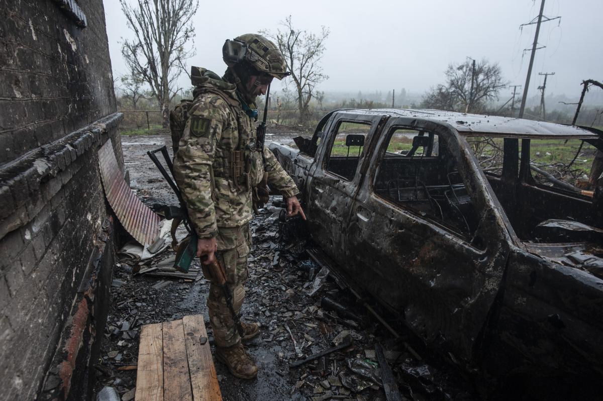 Боєць із позивним “Тринадцятий” показує нерозірвану міну біля спаленого автомобілю. Листопад 2022 р.